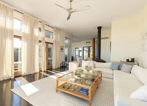 A spacious living room with a large sofa, a glass coffee table, and a ceiling fan.