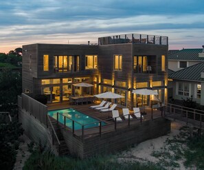 A modern multi-story house with a swimming pool, outdoor seating, and a deck.