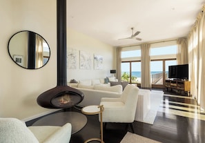 A modern living room with a fireplace, a sofa set, a flat-screen TV, and a view of the ocean.