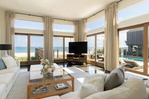 A modern living room with a large TV, comfortable seating, a coffee table, and a view of the ocean.
