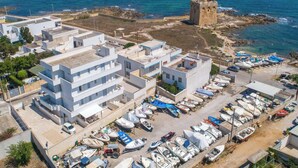 Vista aérea de un pueblo costero con edificios modernos, una torre histórica y un puerto deportivo con barcos.