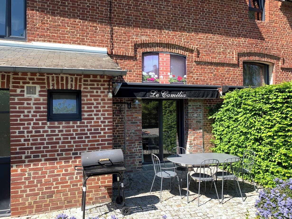 A brick building with a patio area featuring a grill, outdoor seating, and a sign that reads "Le Camélia."