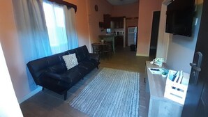 A living room with a black sofa, a dining area with a table and chairs, a kitchen with a microwave and refrigerator, and a TV mounted on the wall. - Cozy 2-bedroom hotel with AC and WiFi in delightful Tela (Tela)