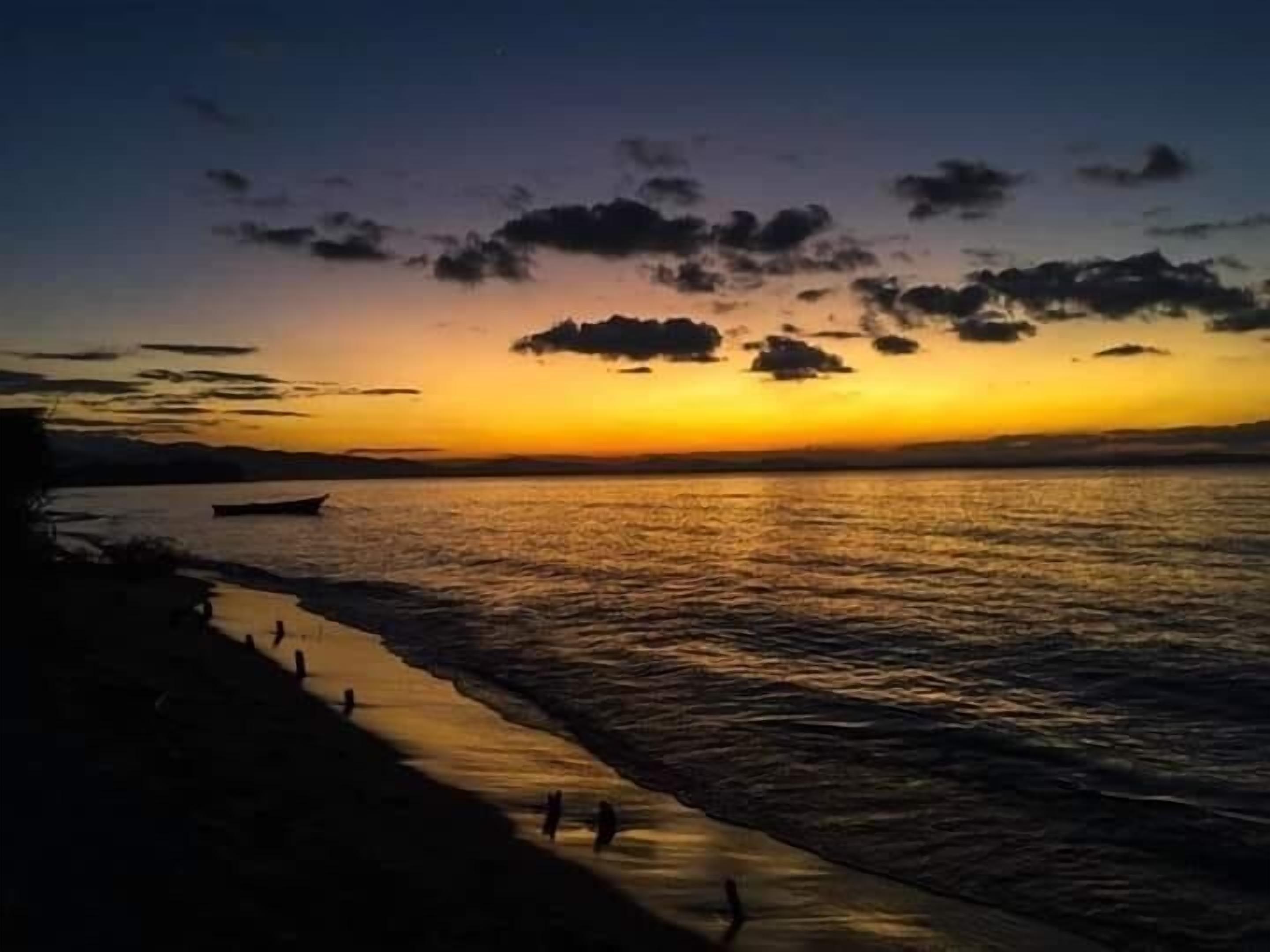 Un coucher de soleil sur une étendue d'eau calme, avec une plage au premier plan.