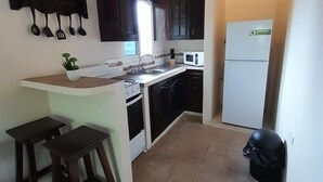 A compact kitchen with dark wooden cabinets, a white countertop, a microwave, a refrigerator, and two wooden stools. - Cozy 2-bedroom hotel with AC and WiFi in delightful Tela (Tela)