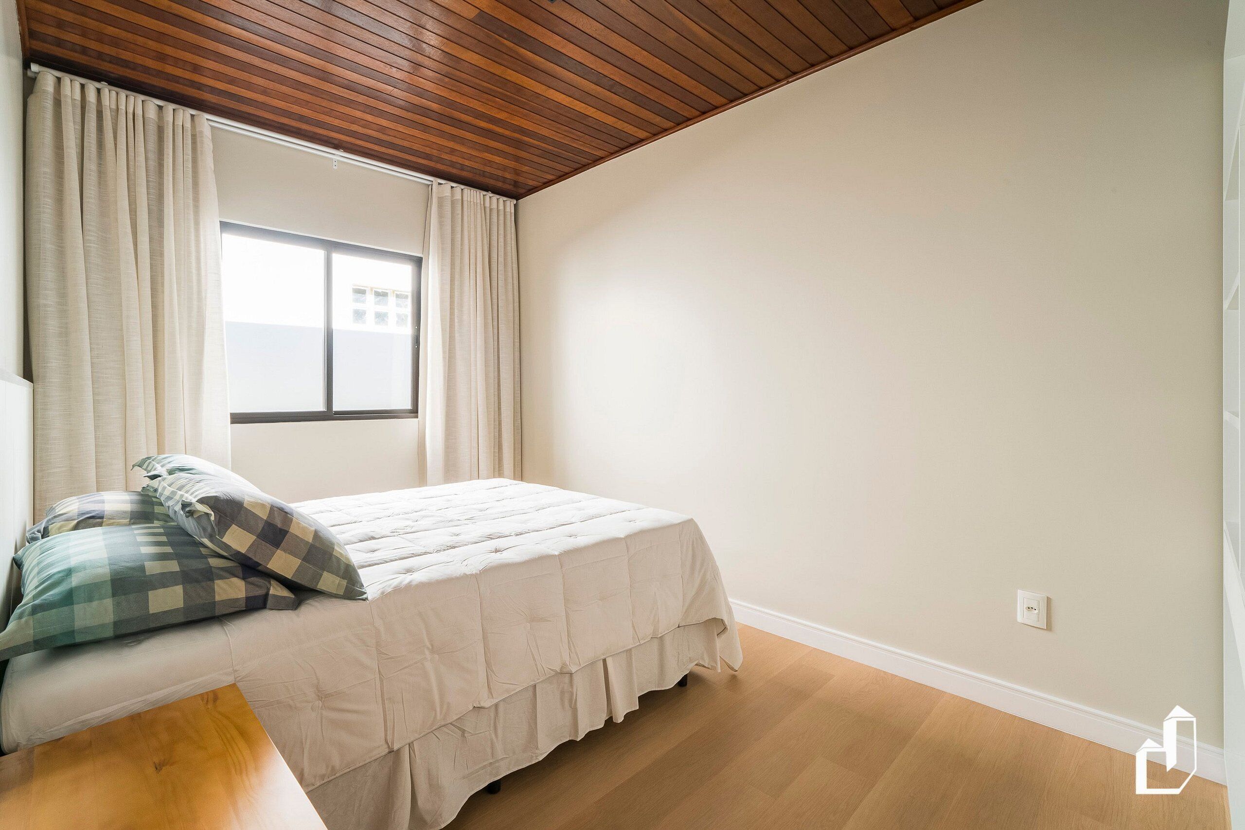 Un dormitorio con cama, cortinas, una ventana y techo de madera.