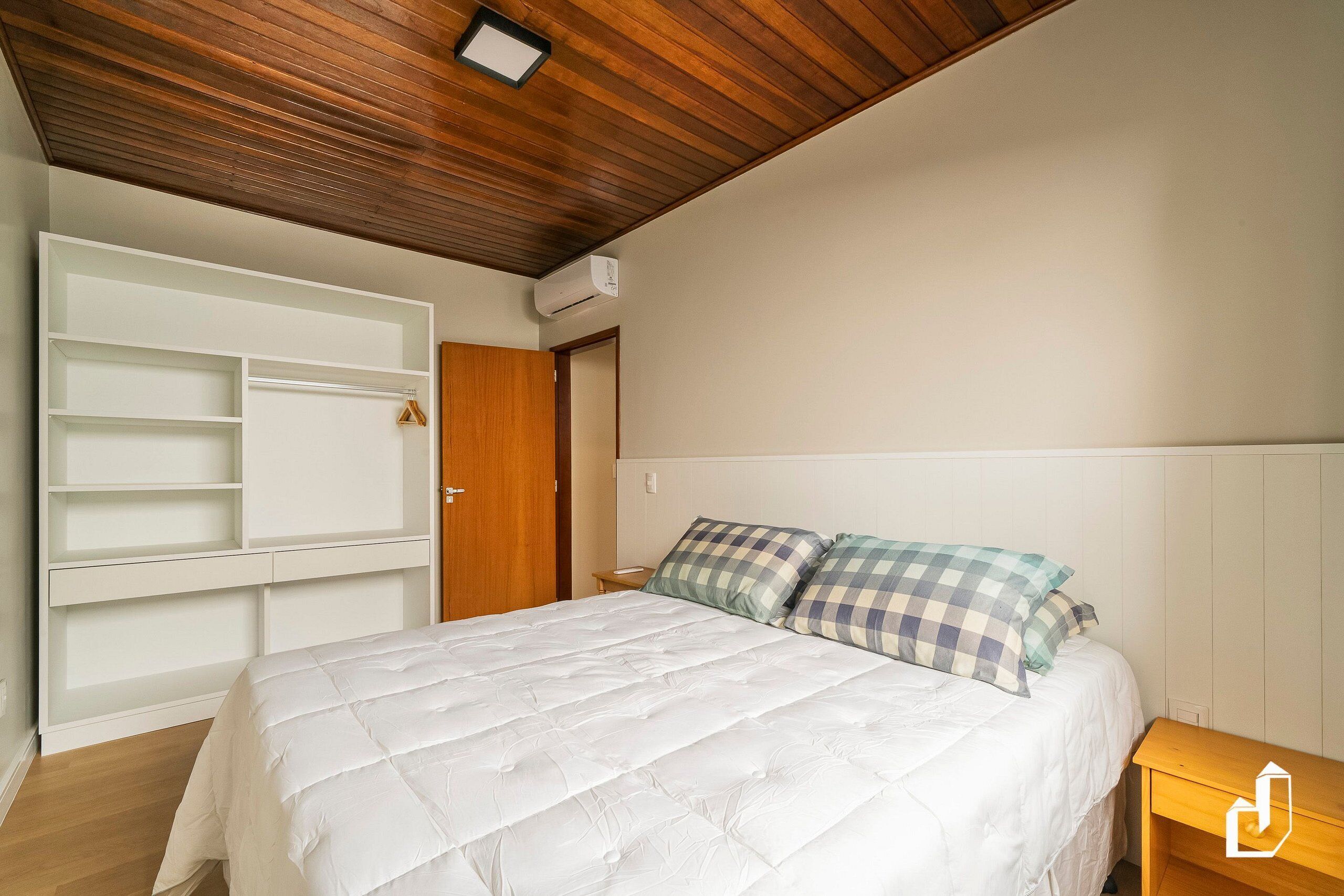 Quarto com cama, guarda-roupa, teto de madeira e ar condicionado fixado na parede.