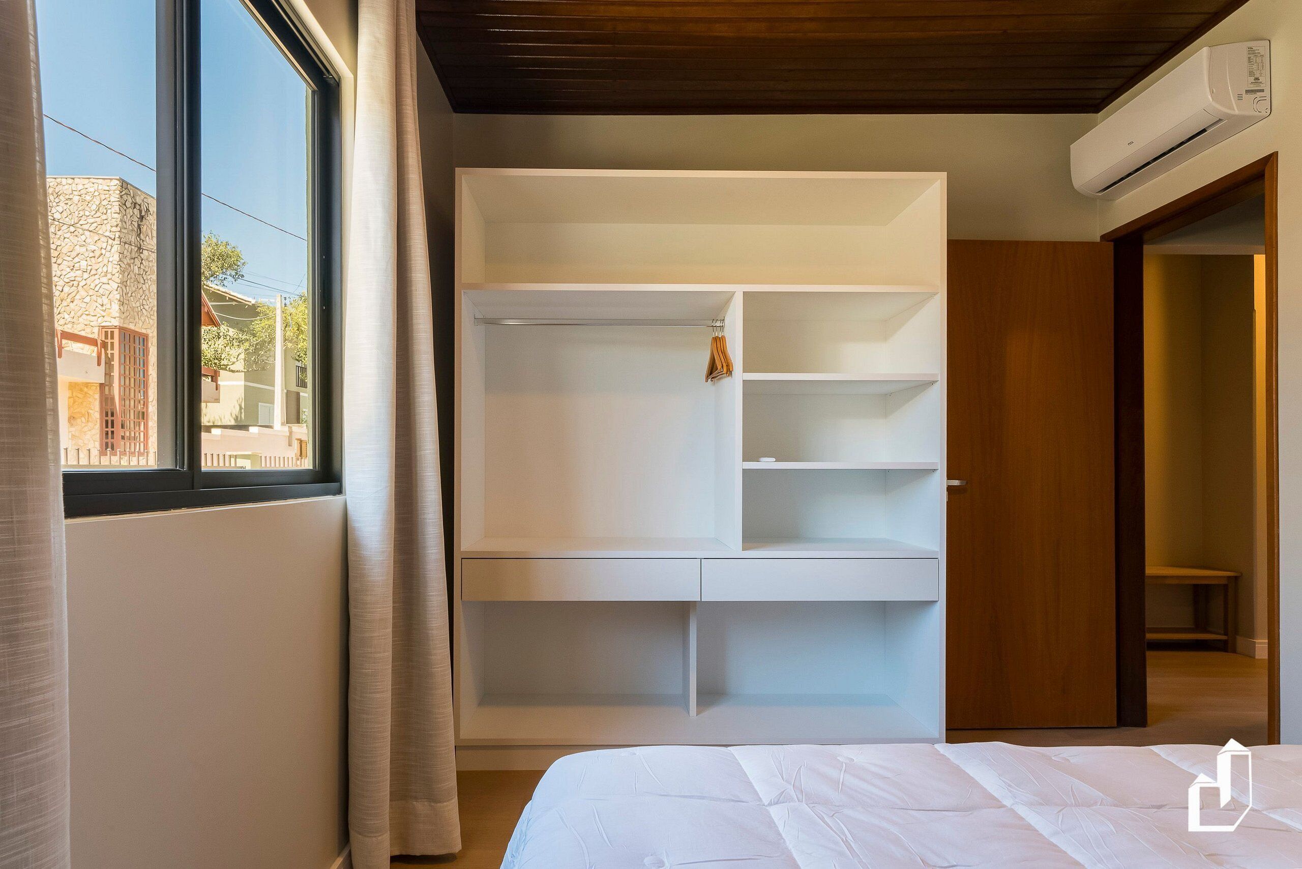 A bedroom with a large window, a built-in wardrobe, and an air conditioning unit.
