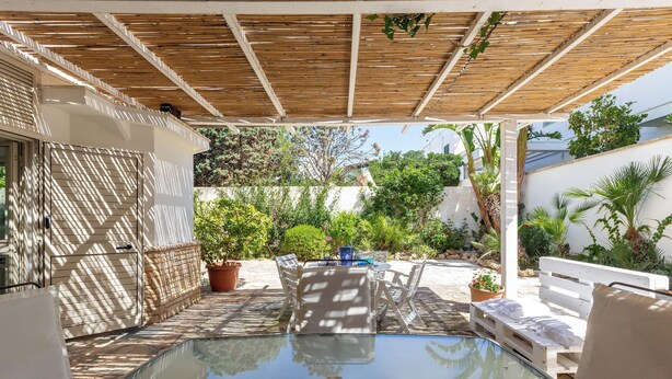 A glass-enclosed pool with a wooden pergola overhead, surrounded by outdoor furniture and potted plants.