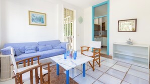 A living room with a blue sofa, a white coffee table, and a wooden chair. There is a white shelf with a decorative item on top.