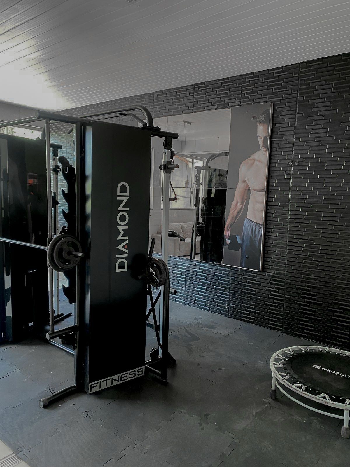 Kuntosali, jossa on painonnostolaite, jonka kyljessä lukee ”DIAMOND FITNESS”, peiliseinä ja trampoliini.