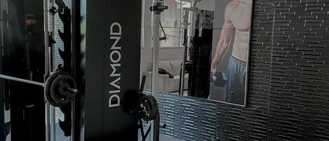 Kuntosali, jossa on painonnostolaite, jonka kyljessä lukee ”DIAMOND FITNESS”, peiliseinä ja trampoliini.