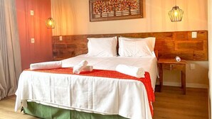 Una cama doble bien hecha con sábanas blancas y una manta roja, cabecera de madera, aire acondicionado montado en la pared y una obra de arte enmarcada sobre la cama.