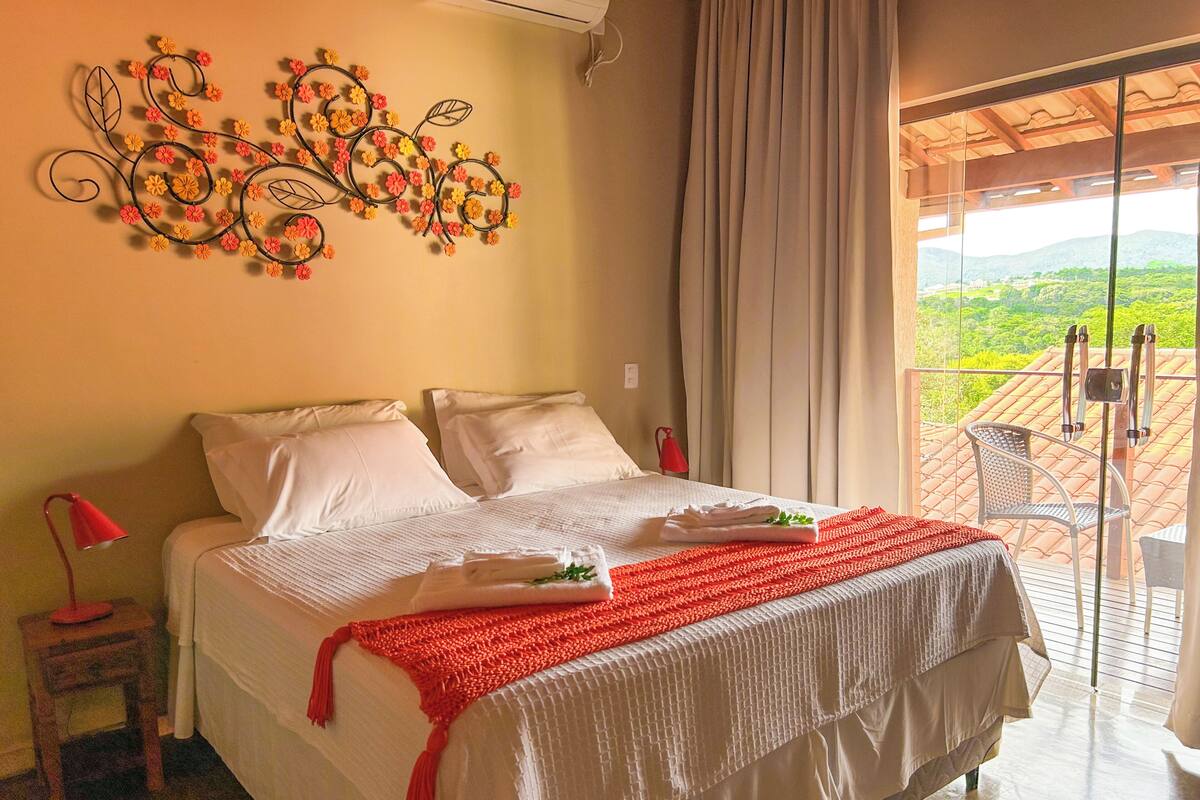 A bedroom with a bed, pillows, a red lamp, a balcony with a view of the countryside.