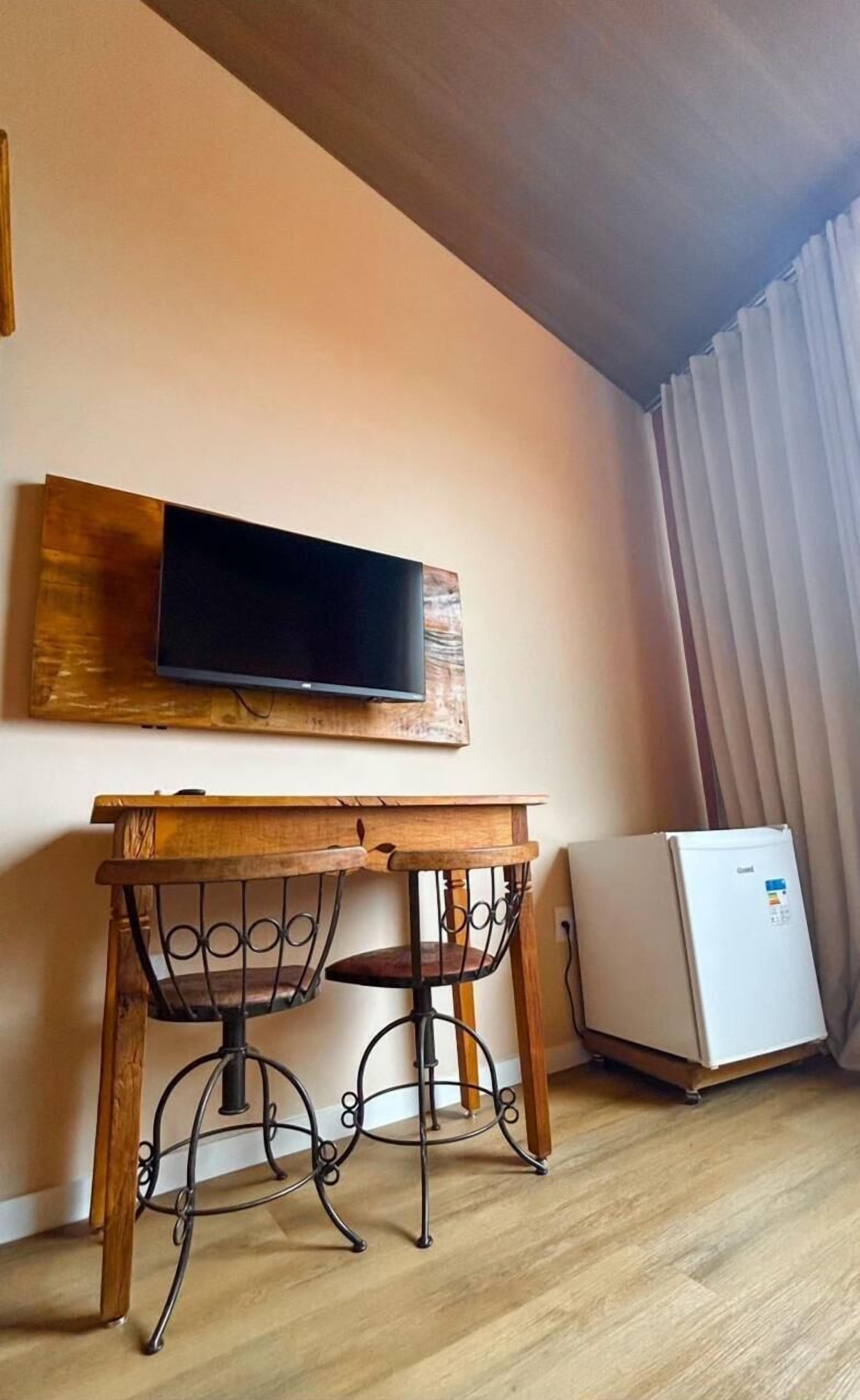 Una habitación pequeña con una mesa y sillas de madera, un televisor montado y un refrigerador blanco.