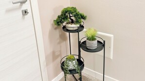 Un présentoir à plantes en métal noir à trois niveaux, avec des plantes en pot disposées contre un mur.