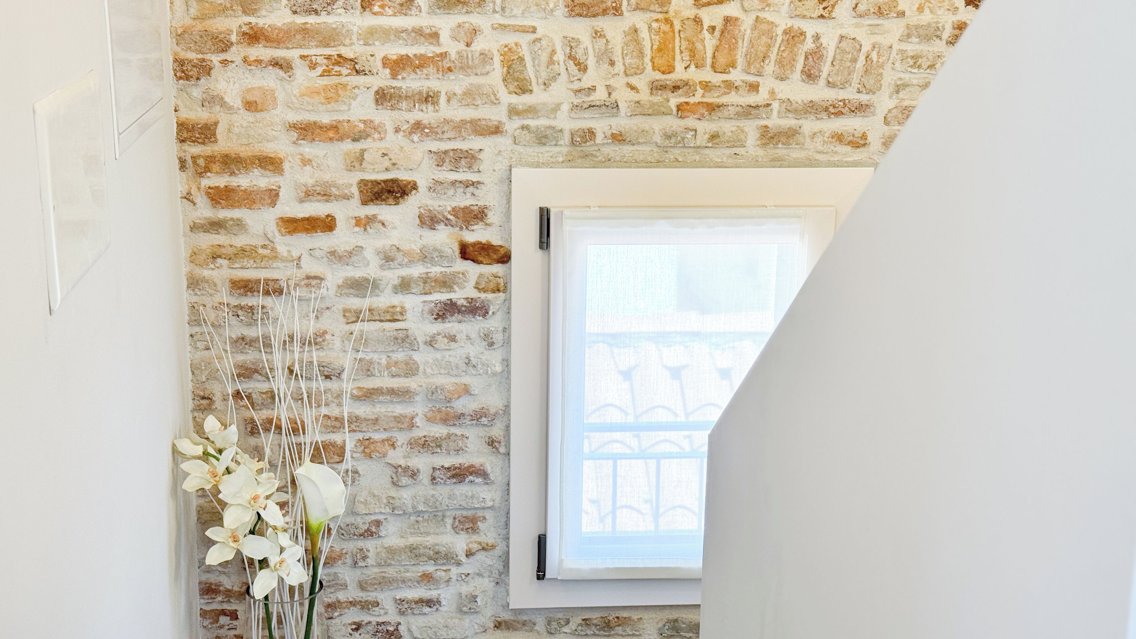 Ein Zimmer mit einer Ziegelwand, einem Fenster mit weißem Rahmen und einer Vase mit weißen Blumen.