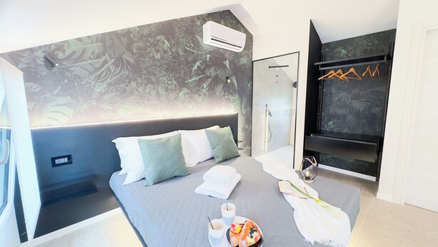 A modern hotel room with a large bed, a flat-screen TV, a shower area, and a tropical-themed wall mural. - Graceful Apartments Hell Apartment by Ca-Sa Check (Chioggia)