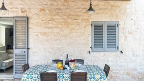 An outdoor dining area with a stone wall, a table set with a tablecloth, chairs, and a bottle of wine. - Casa Alina by Wonderful Italy (Fasano)