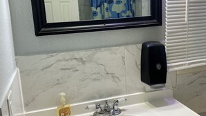 Un baño con lavamanos blanco, un espejo, dispensador de jabón y un perchero para toallas.
