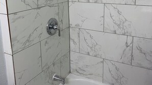 Un baño con baldosas de mármol blanco, una bañera y una ducha con cabezal de ducha manual.