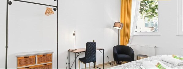 Ett hotellrum med en säng, ett skrivbord, en stol, en lampa och ett fönster med gardiner.