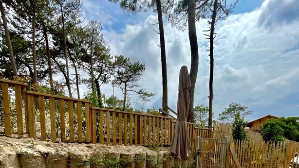 Um deck de madeira com uma mesa posta para dois, cercado por uma cerca de madeira e árvores.