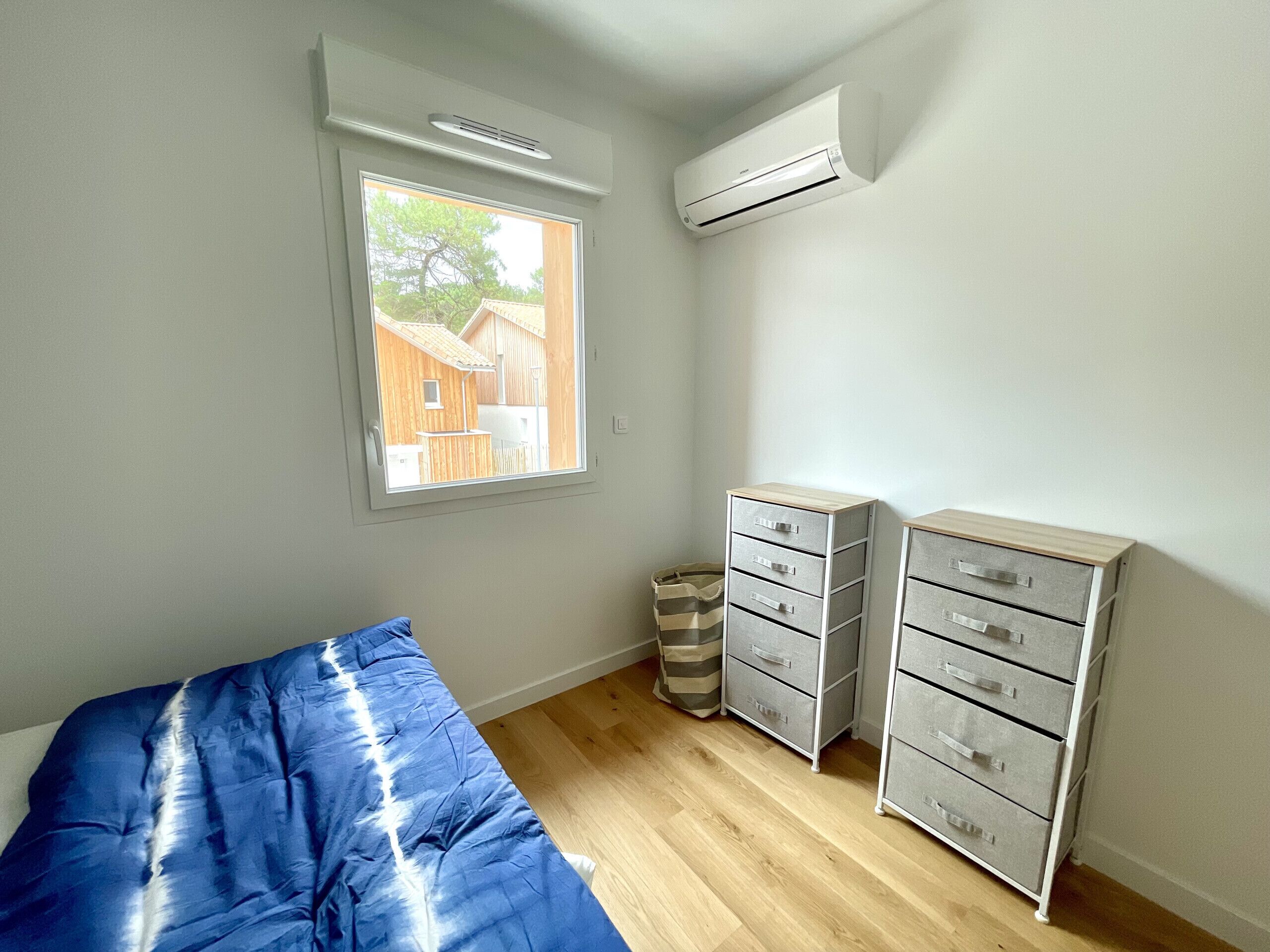 A bedroom with a bed, a window, a wall-mounted air conditioner, and a set of drawers.