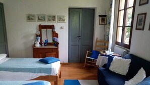 A room with two beds, a wooden dresser, a chair, a table, and a window with curtains. - Elegant private room with lake view balcony (Castelveccana)