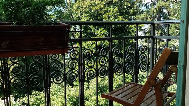 A balcony with a wooden chair and a table, surrounded by a black wrought iron railing. - Elegant private room with lake view balcony (Castelveccana)