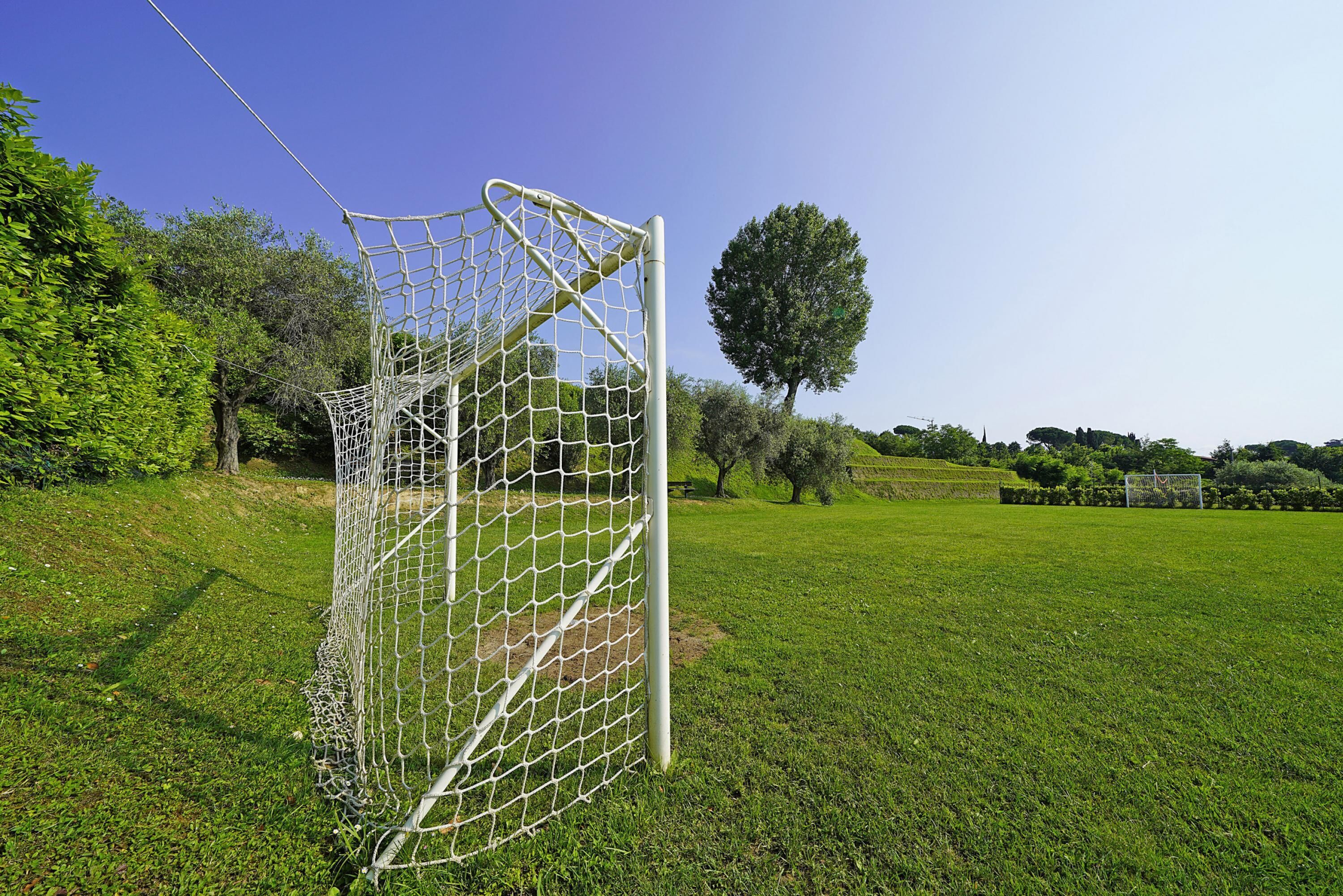 A soccer goal in a grassy field with trees in the background.