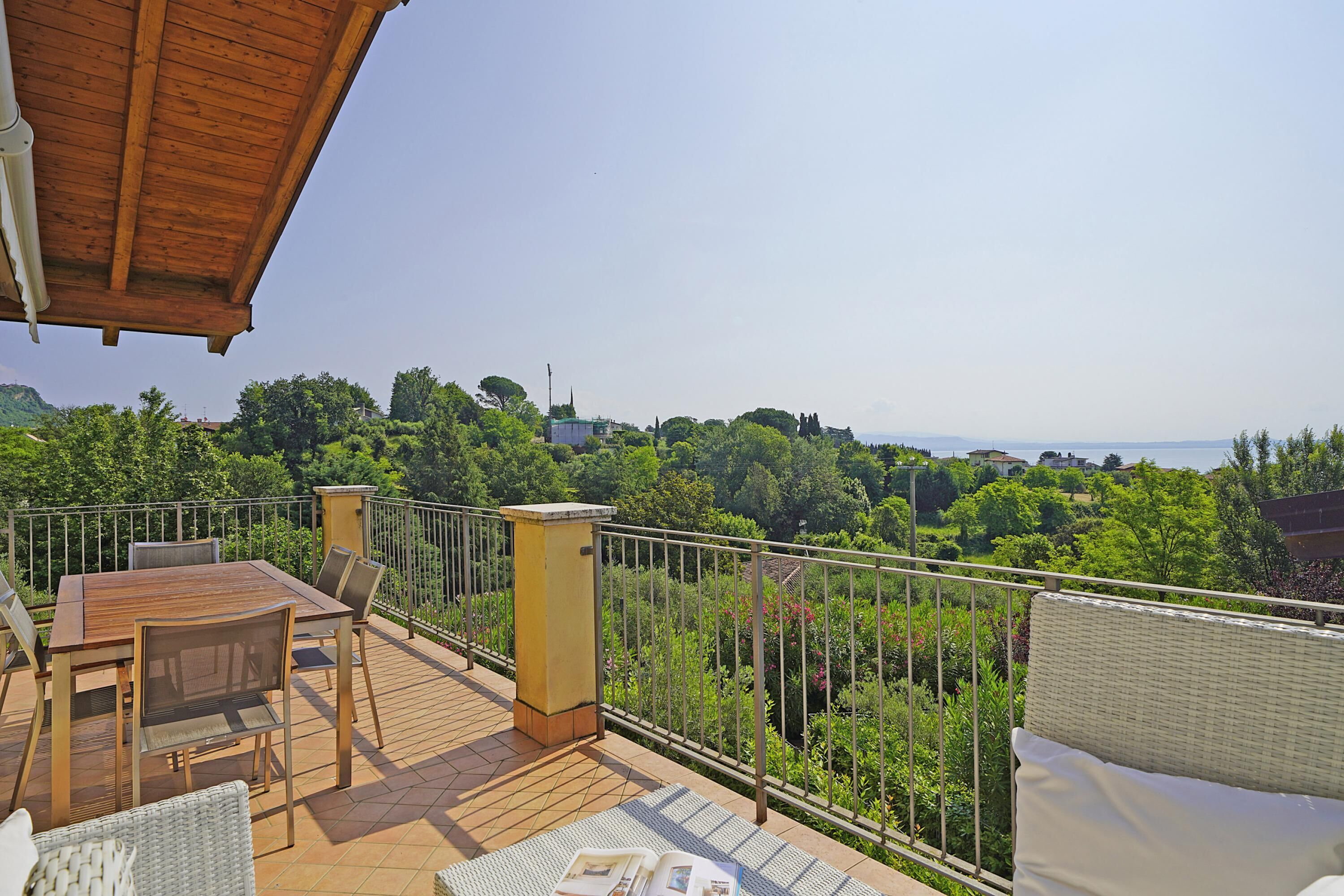 Un balcon avec une table et des chaises en bois, un canapé en osier et une vue sur un paysage verdoyant.