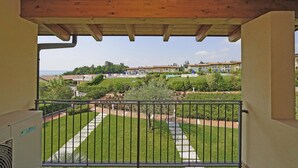 A balcony with a view of a well-maintained garden and residential buildings in the background. - Montecolo Resort E7 by Wonderful Italy (Manerba del Garda)