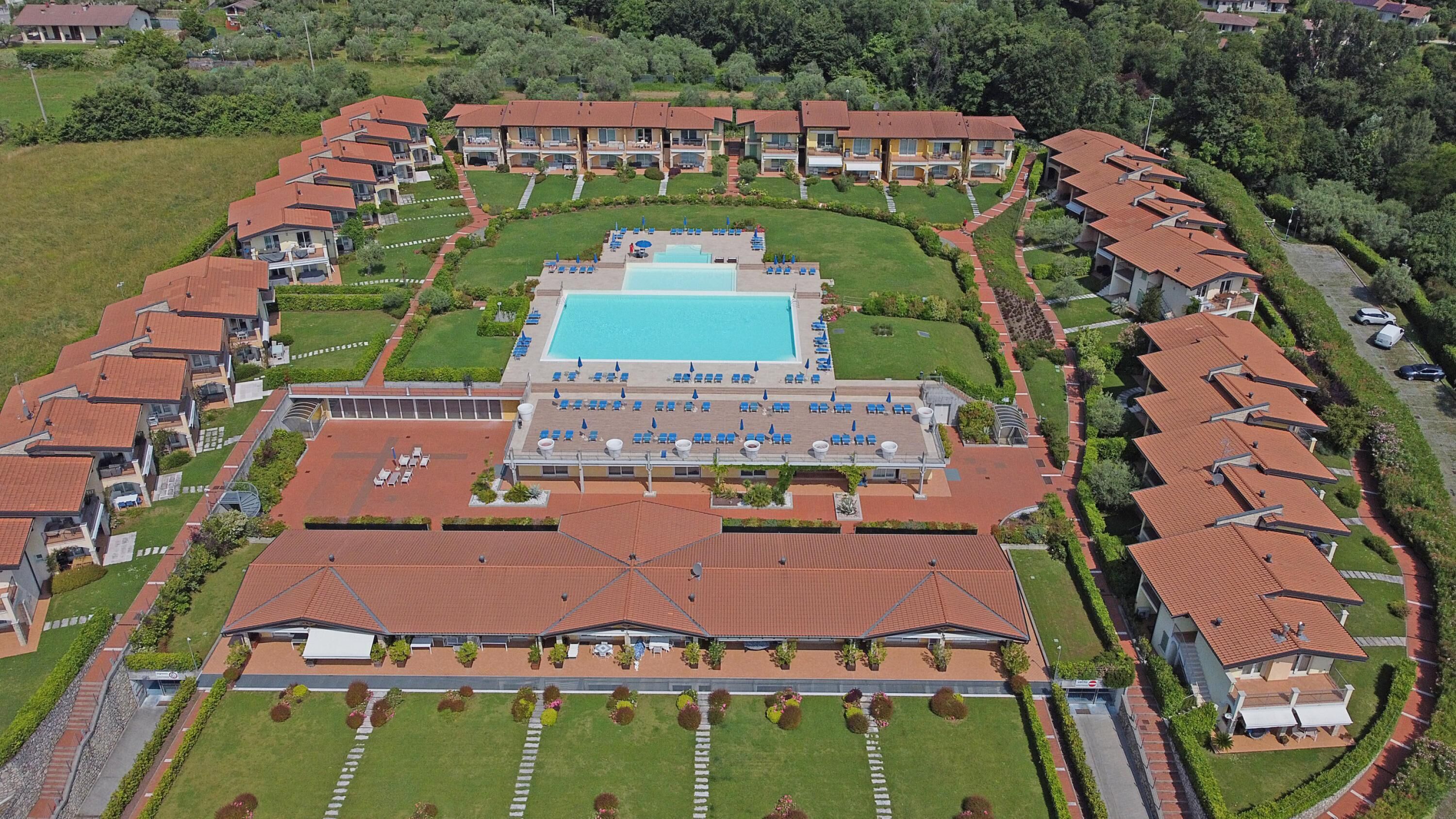 An aerial view of a resort with multiple buildings, a central swimming pool, and well-maintained lawns.