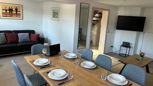 Un comedor con una mesa de madera dispuesta para cuatro, una computadora portátil negra y un televisor montado en la pared.