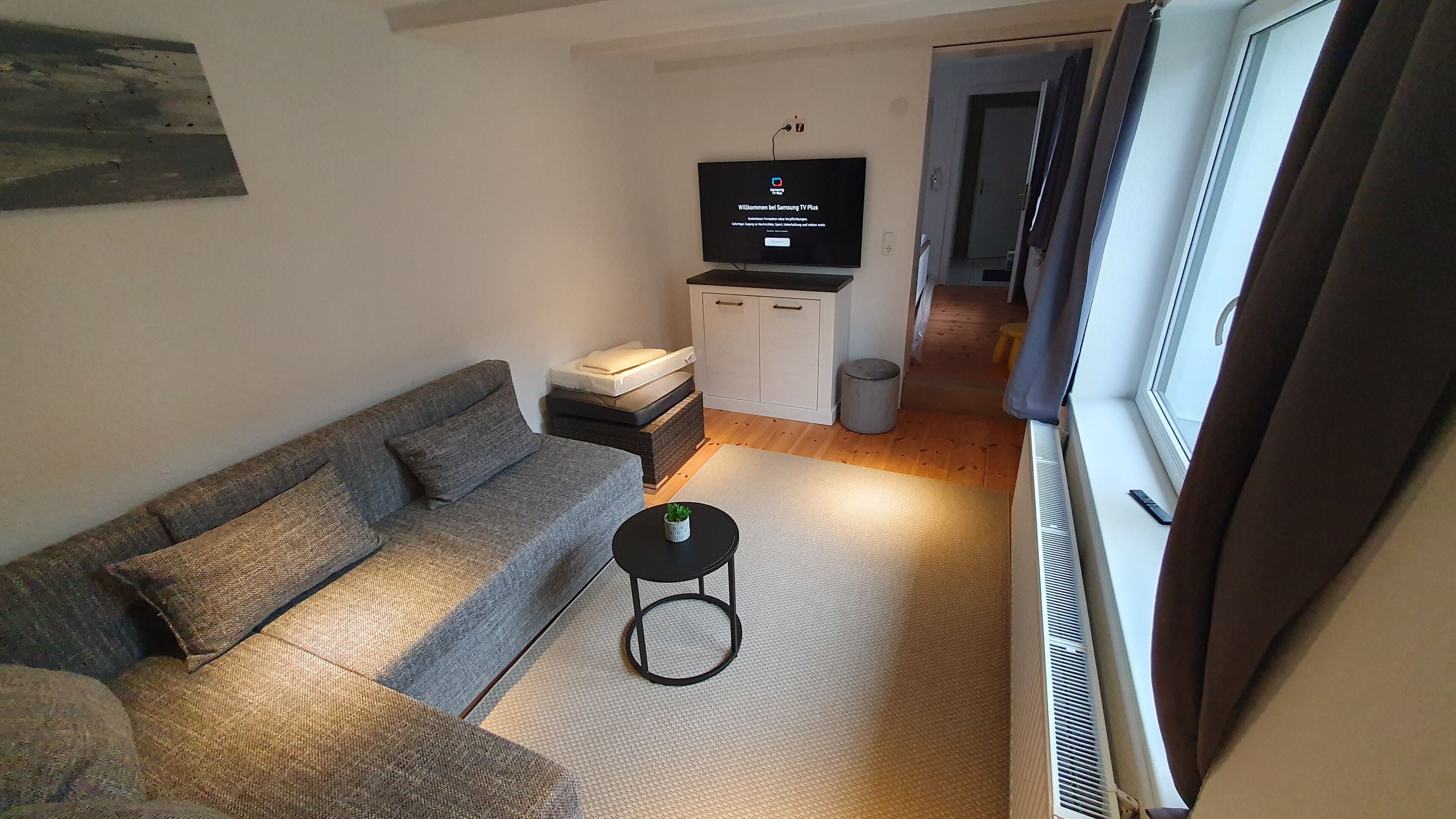 Un salón moderno con un sofá gris, una mesita auxiliar negra y un televisor sobre un mueble bajo.