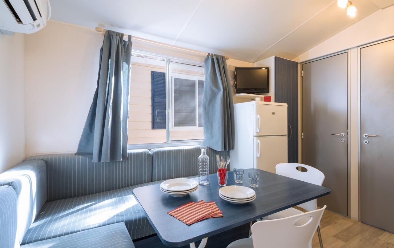 Una kitchenette compacta con comedor, una ventana con cortinas, un televisor y un refrigerador.