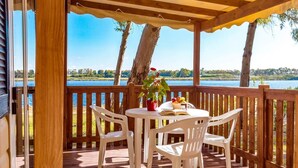 Terraza de madera con mesa y sillas, con vista a un lago.