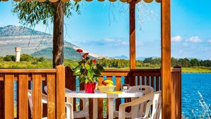 A wooden deck with a table and chairs overlooking a lake, with mountains in the background.