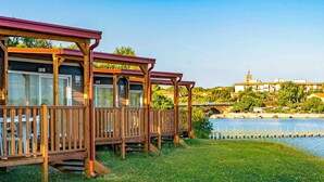 Una hilera de cabañas de madera con balcones, un río y un edificio distante con una torre.