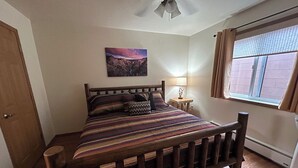 A bedroom with a wooden bed, a nightstand, a lamp, a painting on the wall, and a window with curtains.