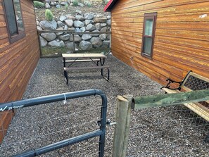 A wooden cabin with a gravel patio, a stone wall, and a wooden bench. - Yellowstone River Hideaway - 1/4 Mile from Yellowstone NP - 1BR Renovated Apartment - Surrounded by Mountains & Overlooking the Canyon (Gardiner)