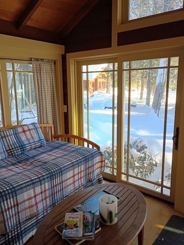A cozy room with a plaid sofa, a wooden table with magazines and a mug, and a large window with a snowy view.