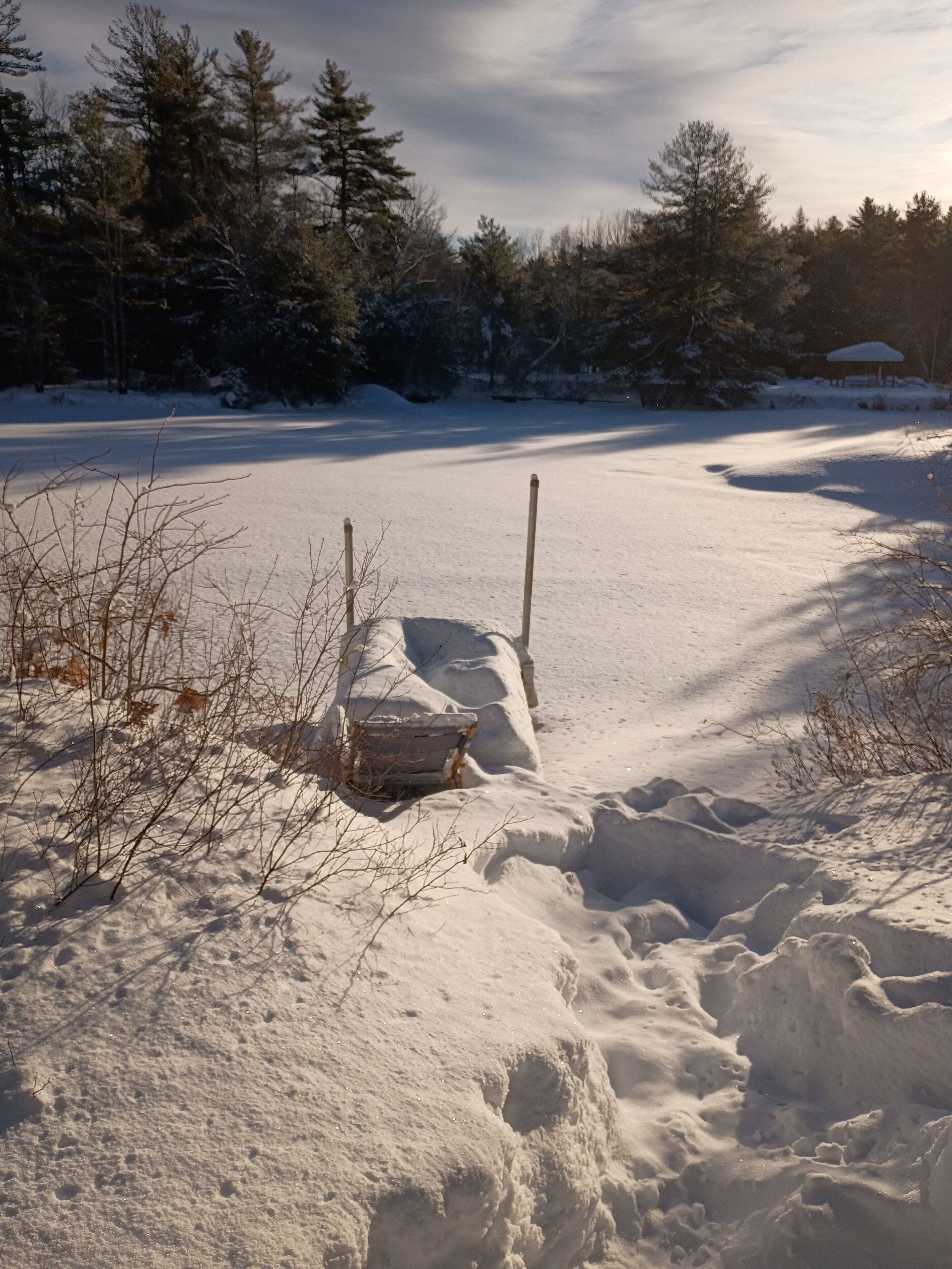 A snow-covered landscape with a wooden bench and a path leading through it.