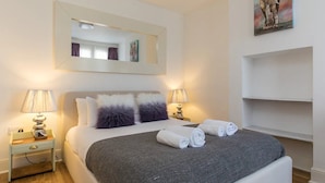 A neatly arranged hotel room with a bed, two bedside tables with lamps, a mirror, and a painting on the wall. - Super Chic Apartment in Beautiful Sunninghill - Pass the Keys (Sunninghill)