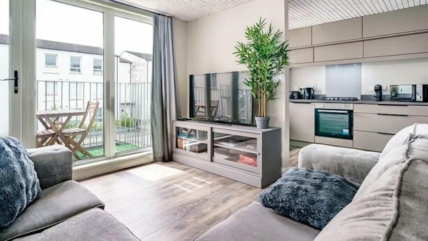 A modern living room with a sofa set, a TV, a potted plant, and a sliding glass door leading to a balcony. - Historical West Belfast | 5 Mins to City Centre - Pass the Keys (Belfast)