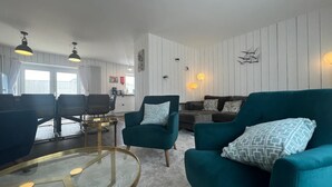 Ein modernes Wohnzimmer mit türkisfarbenen Sofas, einem Glastisch und Pendelleuchten.