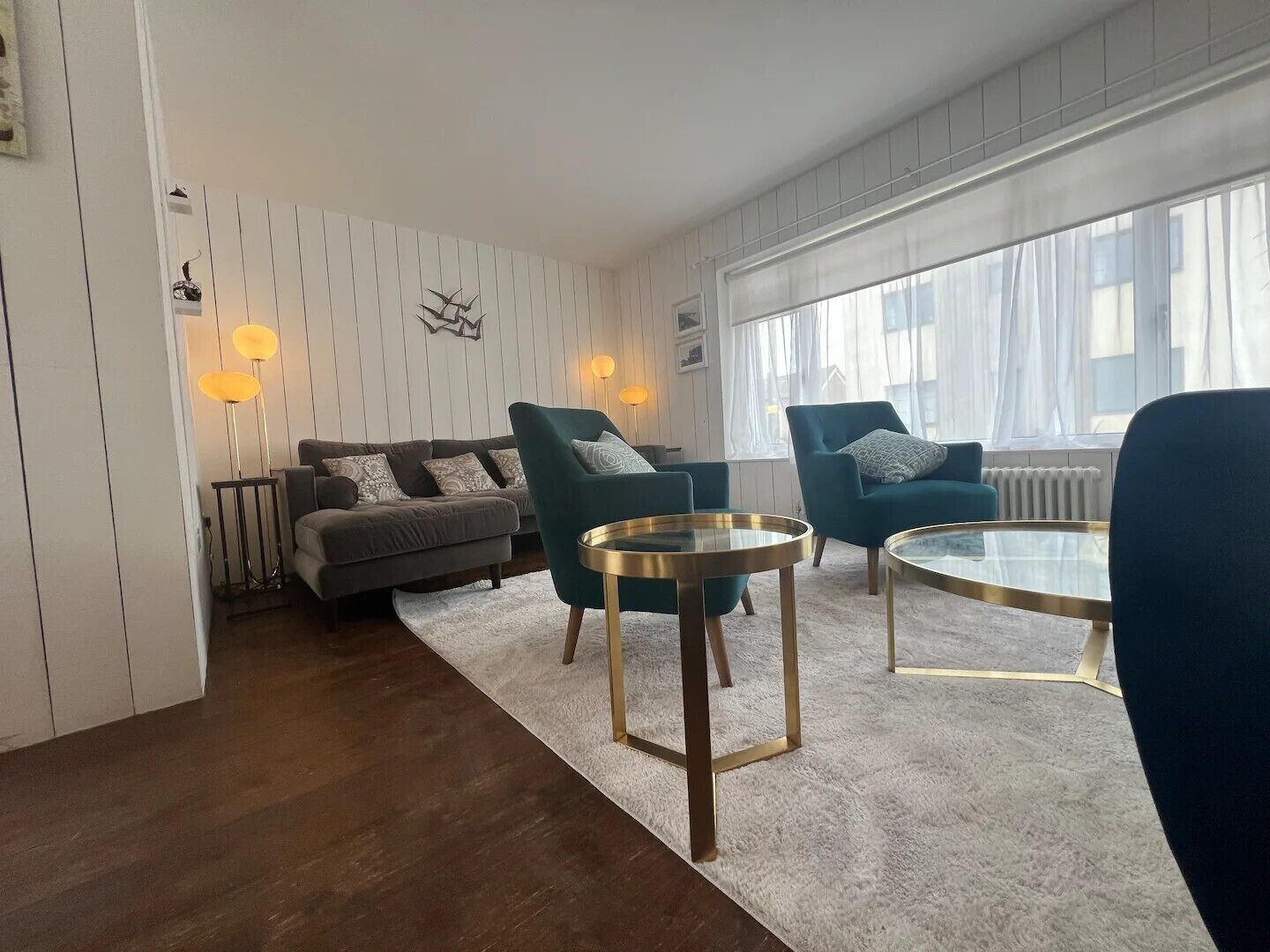 A modern living room with a grey sofa, teal armchairs, and a glass coffee table.