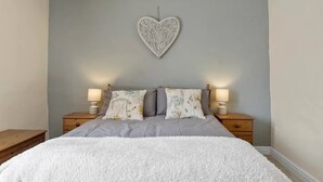 A bedroom with a bed, two bedside tables with lamps, and a wall-mounted heart decoration.