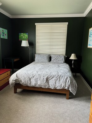 Ein Schlafzimmer mit einem Bett, einem Nachttisch, einer Lampe, einer Kommode und einem Fenster mit Jalousien.